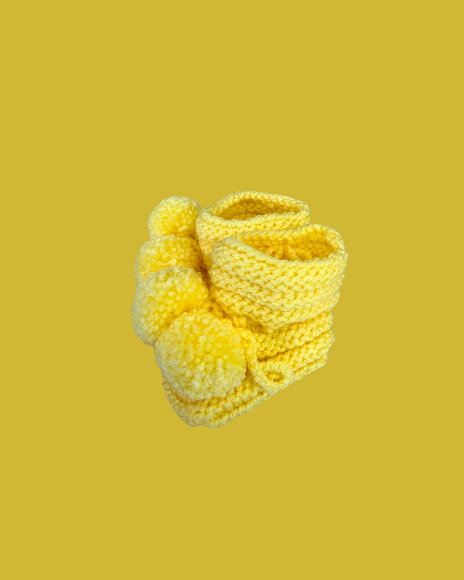 Hand knitted yellow baby booties with soft pom poms for newborns