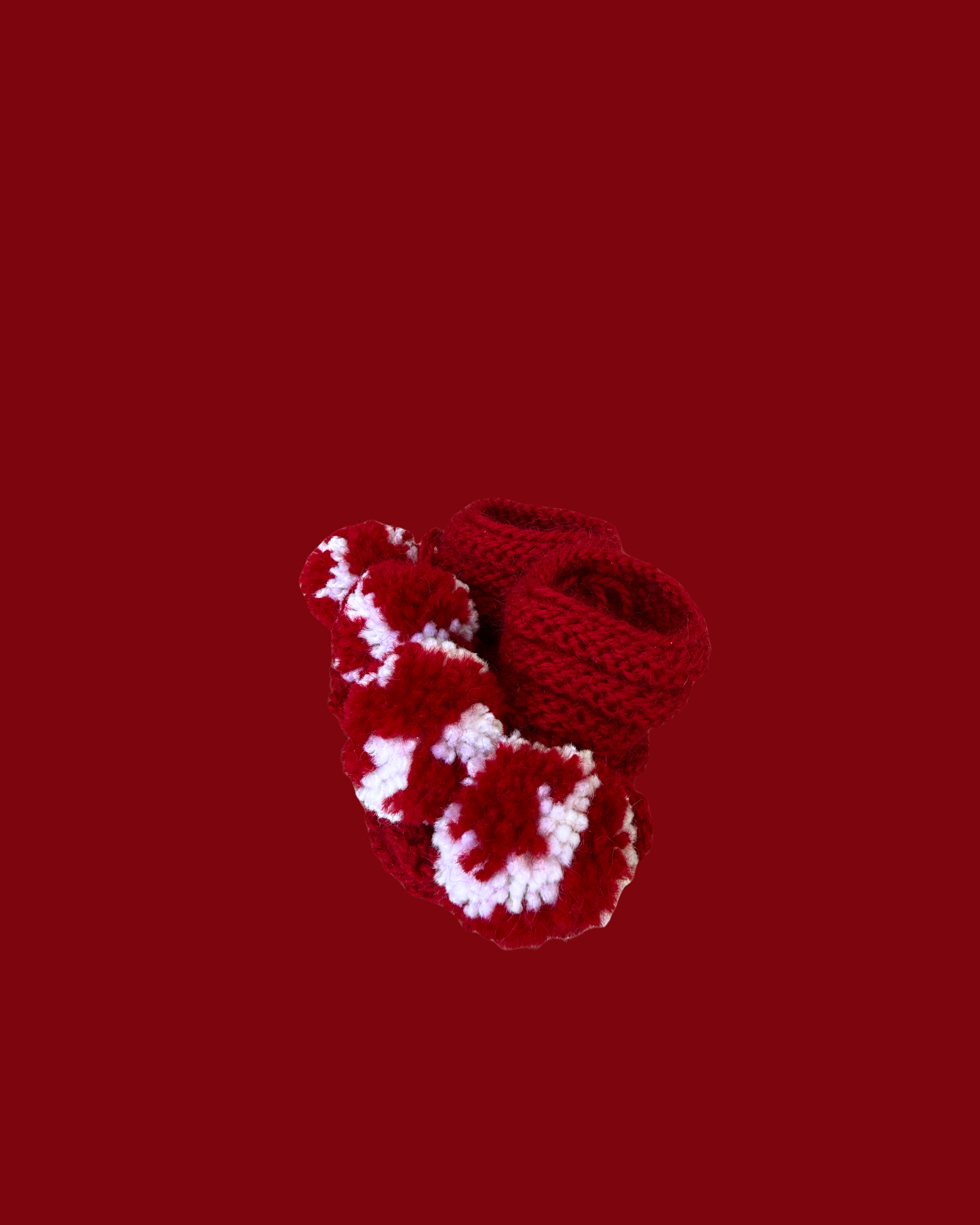 Soft red hand knitted baby booties with decorative white pom poms