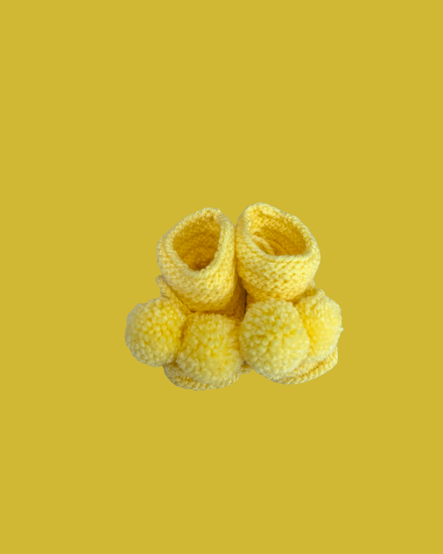 Soft yellow hand knitted baby booties with decorative pom poms